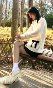 秋日公园里鞠婧祎穿白色毛衣坐在长椅上秀美腿