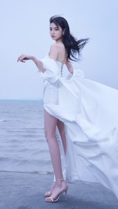 张艺上身穿一身洁白性感的开叉裙站在海边，长腿玉足马上开始舔屏